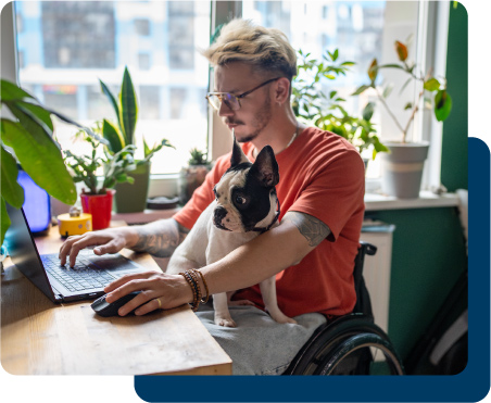 Nonprofit employee working at a computer with a dog on his lap.