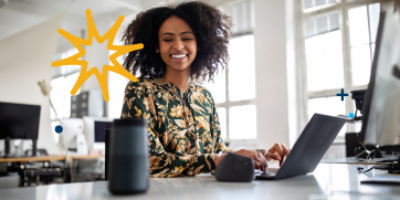 A woman is speaking to an home personal assistant while typing in an office setting.