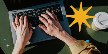 Two hands are typing on a computer with a to go coffee cup sitting to its right.