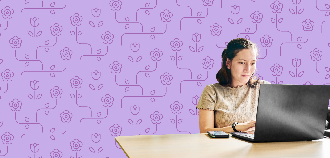 Woman in casual clothing working at a computer with a flower pattern in the background.
