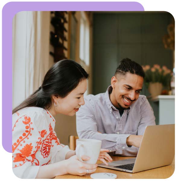 A black man and a Chinese woman sit at a table. They sit behind a laptop and look relaxed and have a lighthearted discussion. The man points at the computer screen.