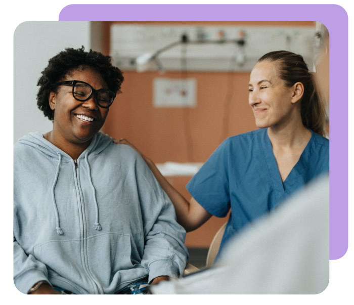 Smiling female nurse consoling happy patient sitting with doctor during consultation at hospital - stock photo