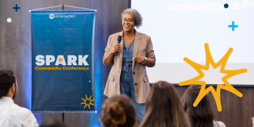 A woman speaking in front of a crowd with a SPARK banner next to her.