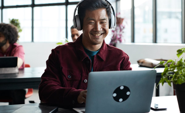 Smiling businessman wearing wireless headphones while using laptop at desk in office