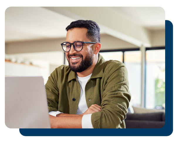 Smiling young Indian man sitting at home while using laptop. Multiethnic business man attending meeting online at home while using laptop. Happy mixed race man wearing eyeglasses while using laptop during work from home with copy space.