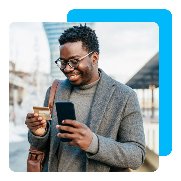 Middle age Afro American businessman standing on street and using smart phone and bank credit card for online payment.