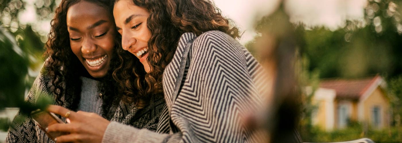 Lady referring friend to DonorPerfect both smiling looking at phone to check out cool features