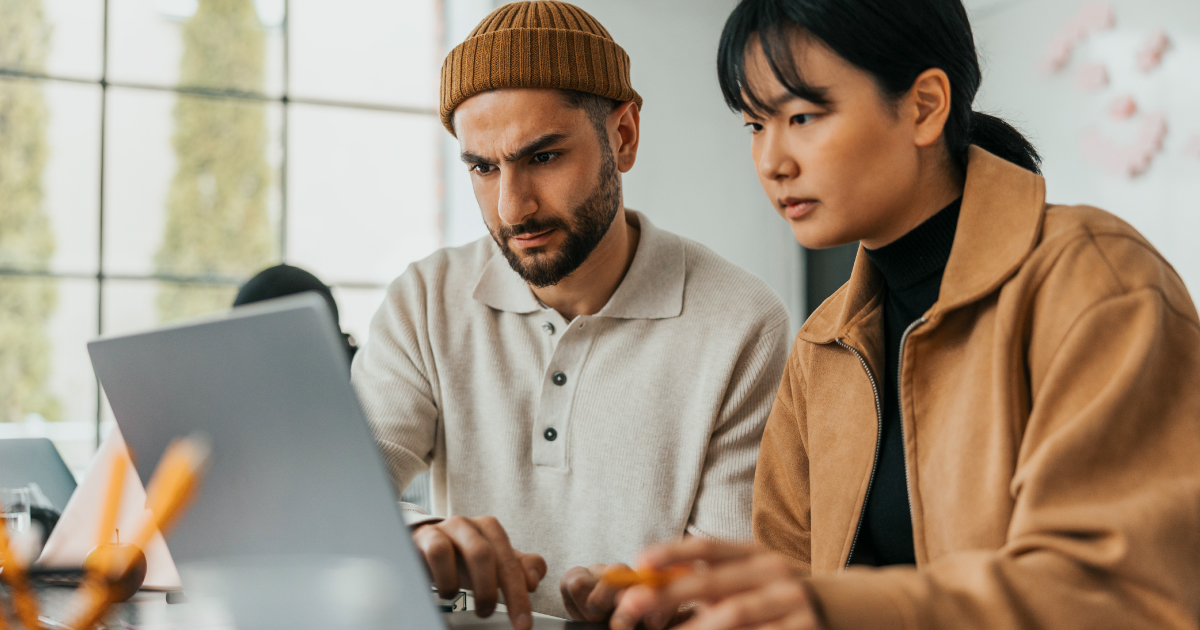 One person helping another while working in a computer in an office setting