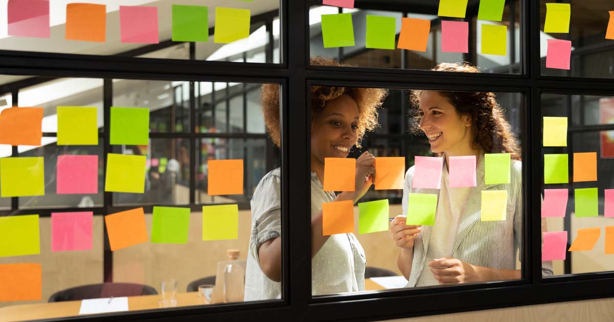 Two women behind a window looking at sticky notes on the window