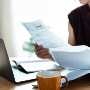Cropped shot of Asian woman sitting at dining table, handling personal finance with laptop. She is making financial plan and planning budget as she go through her financial bills, tax and expenses at home. Wealth management, banking and finance concept