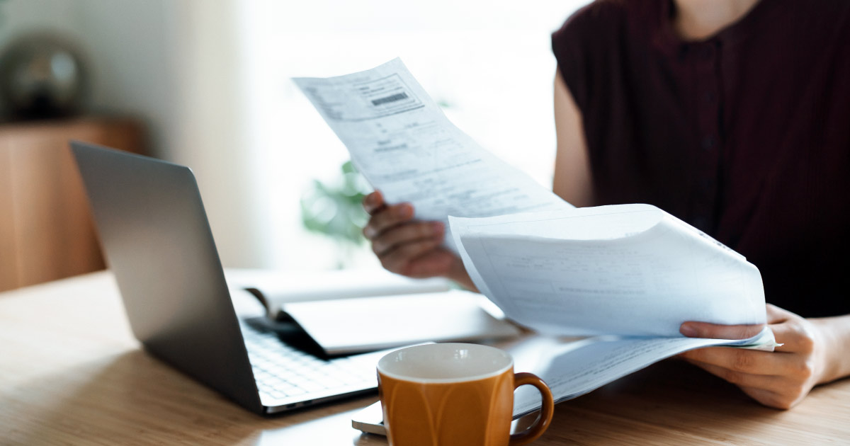 Cropped shot of Asian woman sitting at dining table, handling personal finance with laptop. She is making financial plan and planning budget as she go through her financial bills, tax and expenses at home. Wealth management, banking and finance concept
