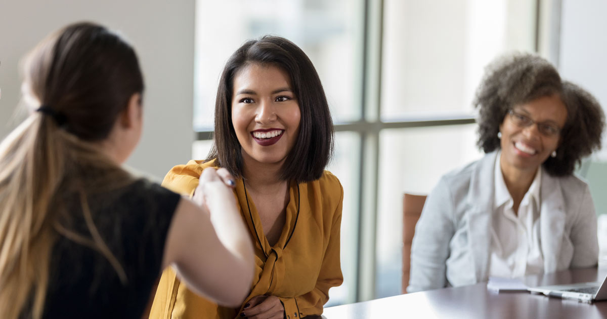 Cheerful mid adult businesswoman greets a colleague with a handshake before a meeting.