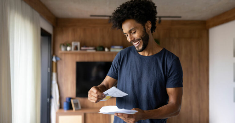 Man standing in his living room excitedly reading a letter from a nonprofit