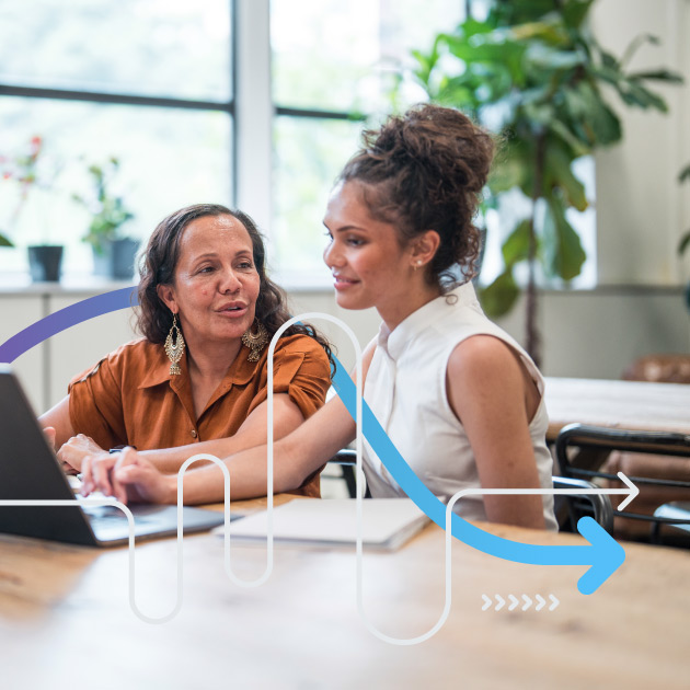 Young adult and mature women, dressed in professional attire, engage in collaborative work at a laptop in a contemporary office