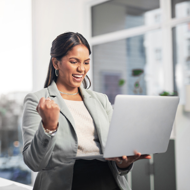 featured image of an attractive young businesswoman standing in the office and celebrating a success while using a laptop