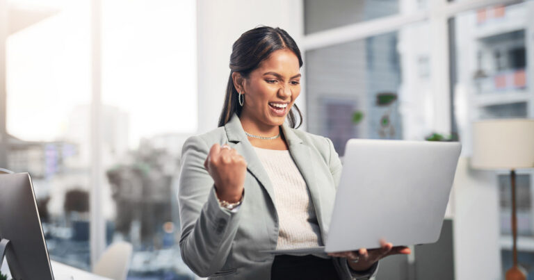 hero image of an attractive young businesswoman standing in the office and celebrating a success while using a laptop