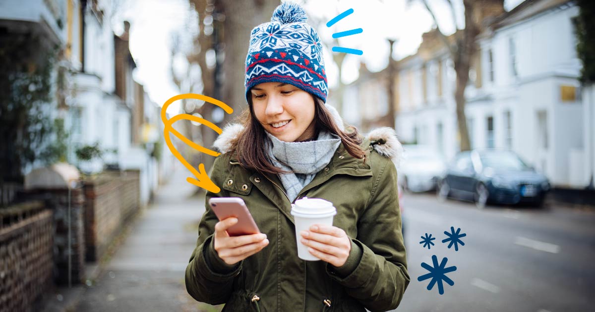 Woman in winter clothing walks down the street while checking her phone