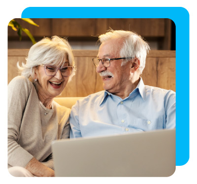 A cheerful senior couple is sitting at home and using laptop.