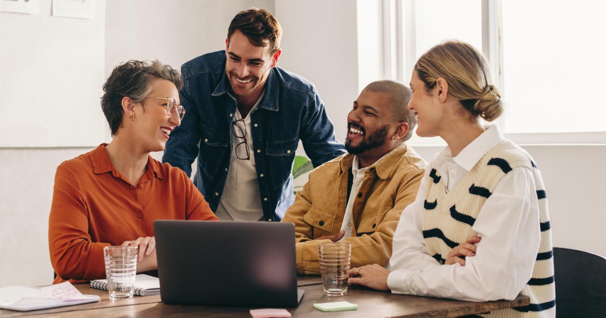 A few coworkers looking at a computer while laughing together in the office.