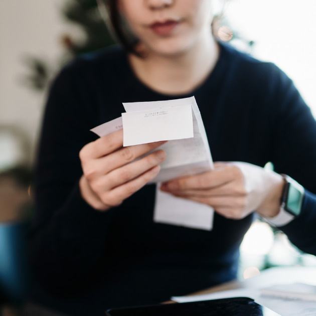 Young Asian woman managing personal banking and finance. Planning budget and calculating expenses with digital tablet while going through various expense receipts at home after shopping. Home finances. Home budgeting. Banking and finance concept