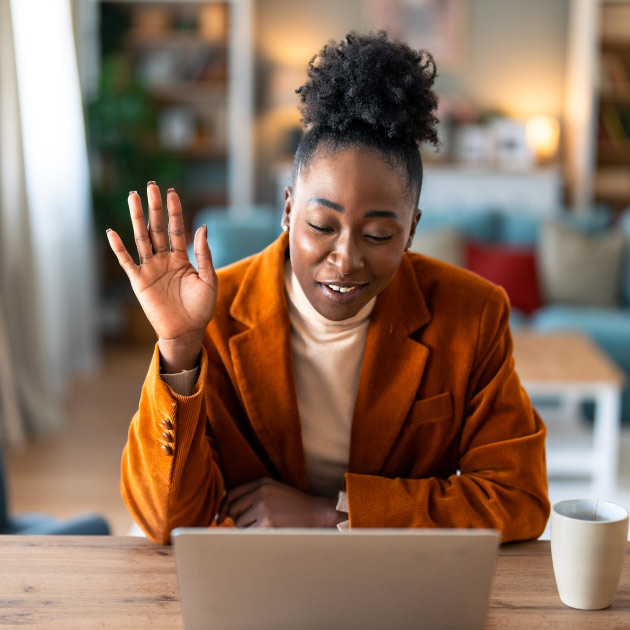 Stylish black woman waving hand during video call on laptop in living room at home.