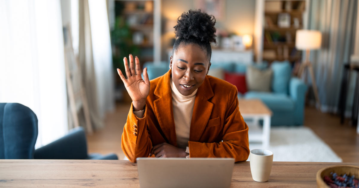 Stylish black woman waving hand during video call on laptop in living room at home.