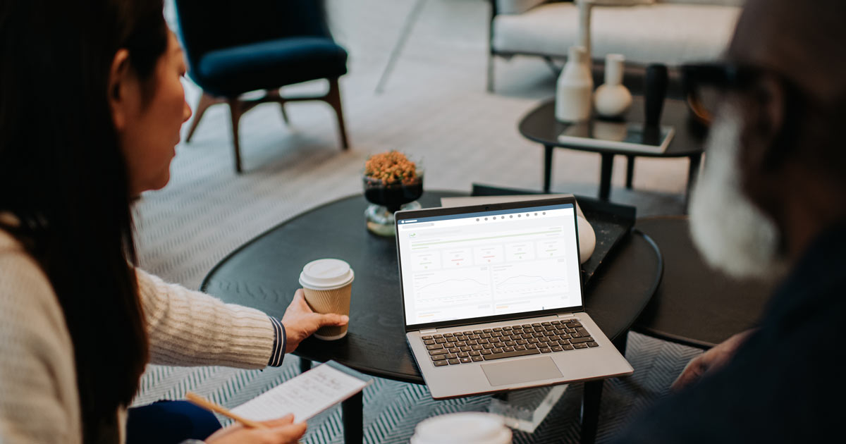 Coworkers look at a laptop together as they drink takeaway coffees