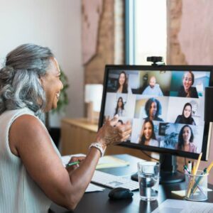 A serious senior businesswoman gestures as she facilitates a staff meeting while working from home. She is talking with her colleagues during a video conference.