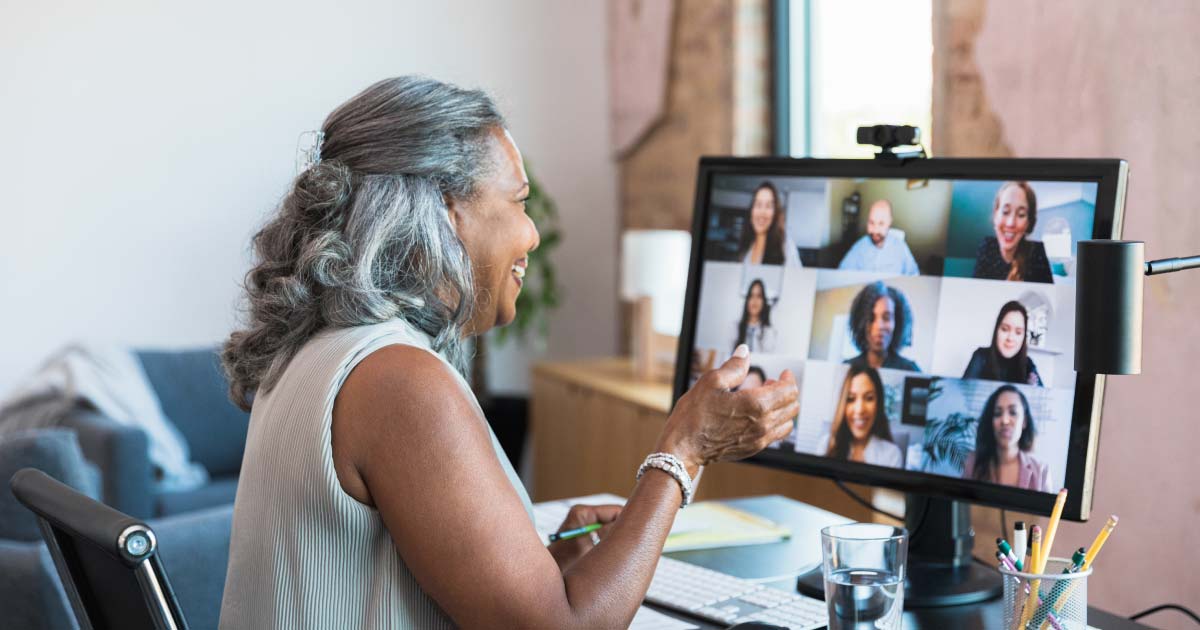 A serious senior businesswoman gestures as she facilitates a staff meeting while working from home. She is talking with her colleagues during a video conference.