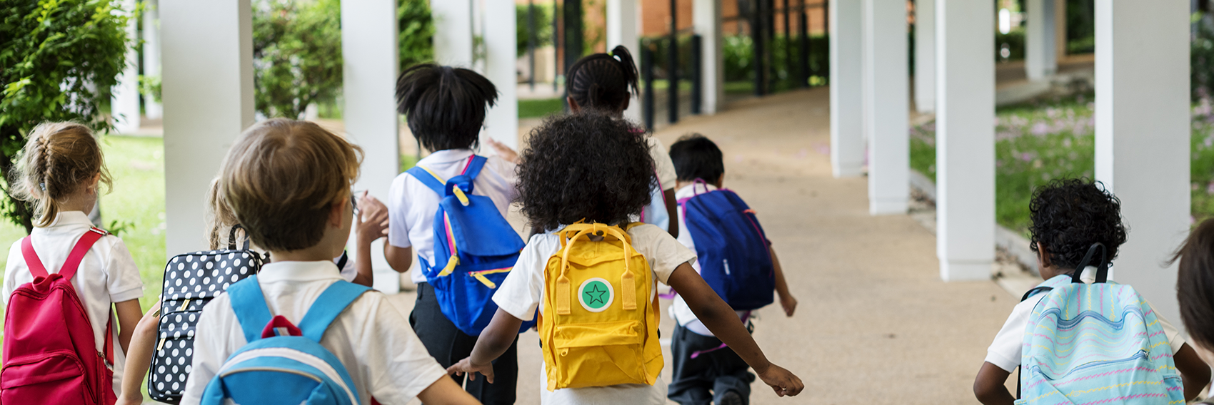 children in colored backpacks running toward school - Rediker Software hero image
