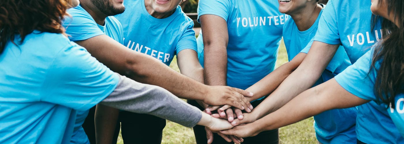 A group of volunteer with the same shirt with their hands in a scrum.