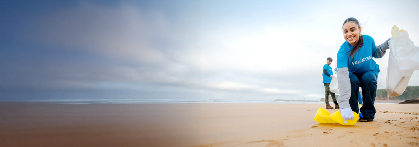 portrait of young latina girl picking up plastics on a beach with a team of cleanup volunteers