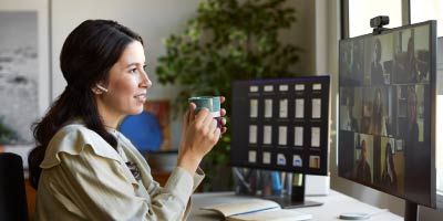 Businesswoman having coffee during video call. Female professional is using computer at desk. She is in home office.